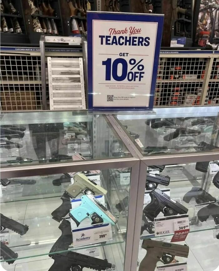 Guns displayed in a store with a sign offering teachers a 10% discount; humans-of-capitalism-pictures theme.