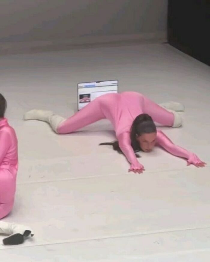 Performance art of humans in pink suits, stretching on a white floor, highlighting humans-of-capitalism-pictures theme.