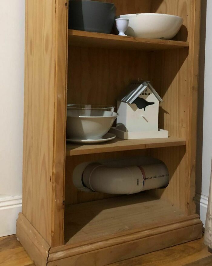 Wooden shelf with a plumbing pipe awkwardly installed through the bottom shelf, exemplifying a design disaster.