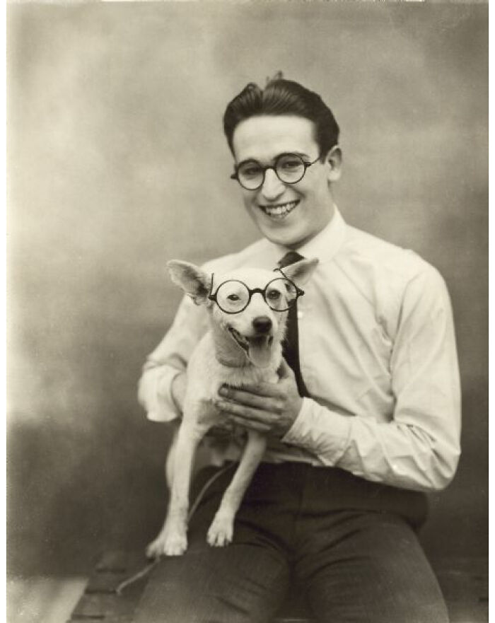 Portrait Of Harold Lloyd Sitting And Holding His Dog Specks In His Lap. The Dog And Harold Are Wearing Matching Eyeglasses. Date Unknown