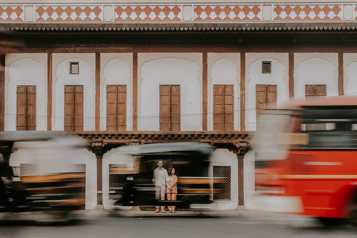 Couple standing still in front of a traditional building as traffic blurs by, capturing a destination wedding moment.