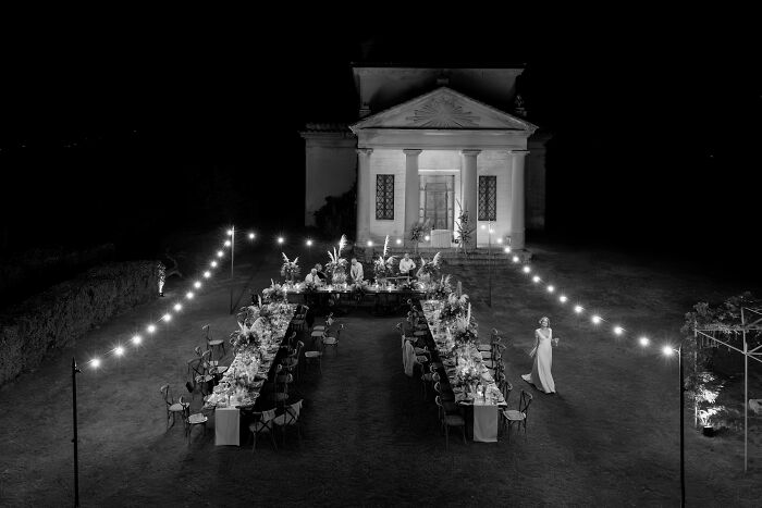 Outdoor destination wedding scene in front of a historic building with string lights and elegant table setting.