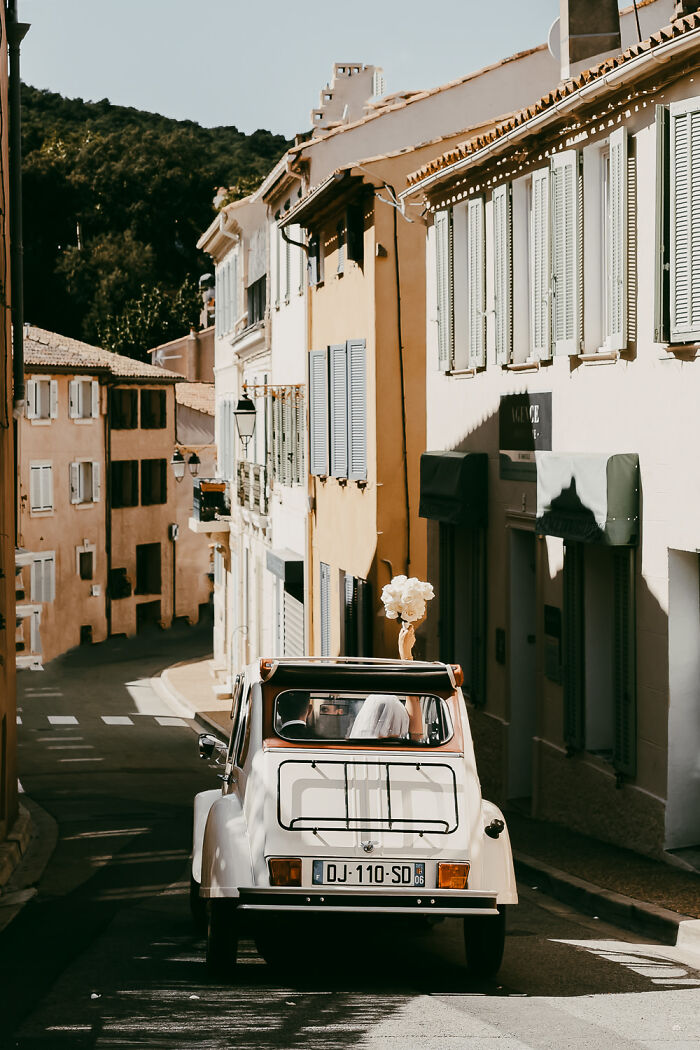 Vintage car with a couple in wedding attire driving through a charming street, showcasing destination wedding photography.