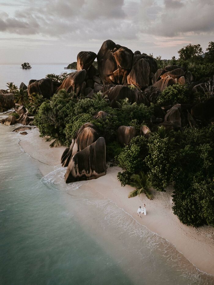 Couple walking on a beach surrounded by lush greenery and large rocks, showcasing the best destination wedding photo.