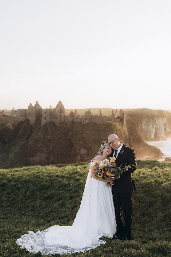 Couple embraces with bouquet in front of castle ruins at sunset, top destination wedding photo of 2024.