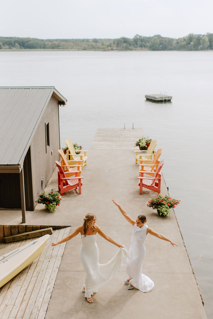 Couple dancing on a lakeside dock, celebrating their destination wedding in elegant white dresses.