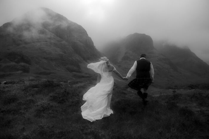 Couple holding hands in wedding attire, running through misty mountains; top destination wedding photo of 2024.