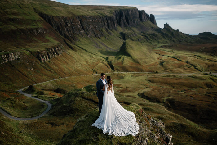 Couple at a stunning destination wedding setting, with dramatic cliffs and sweeping green landscapes in the background.