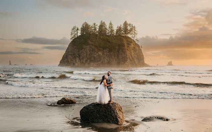 Couple embraces on a rock at sunset for destination wedding photos, with ocean and island backdrop.