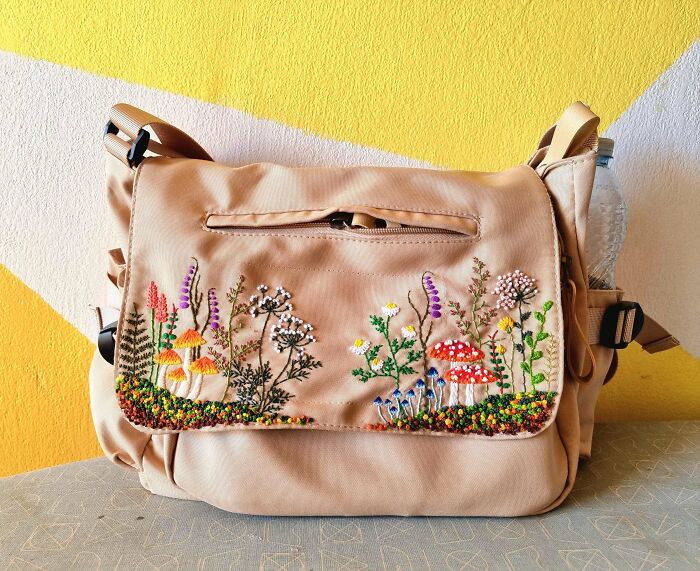 Creative embroidery of colorful mushrooms and plants on a beige bag against a yellow and white background.