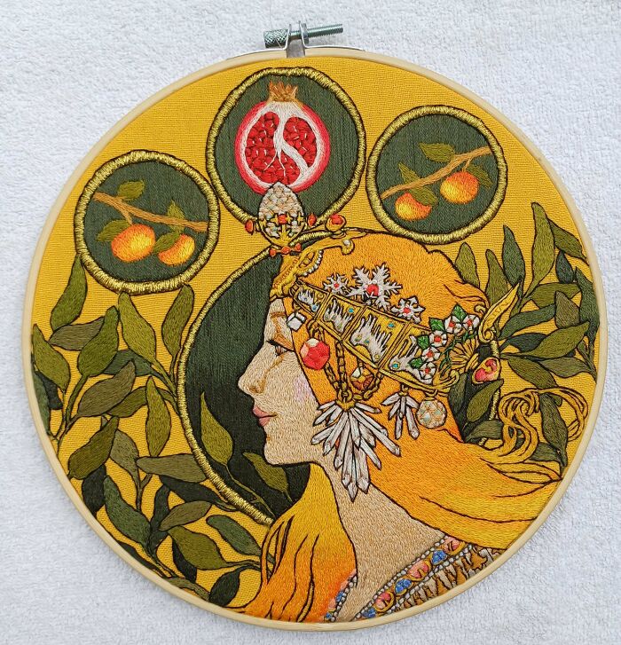 Intricate embroidery art featuring a creatively designed profile of a woman adorned with foliage and fruit motifs.