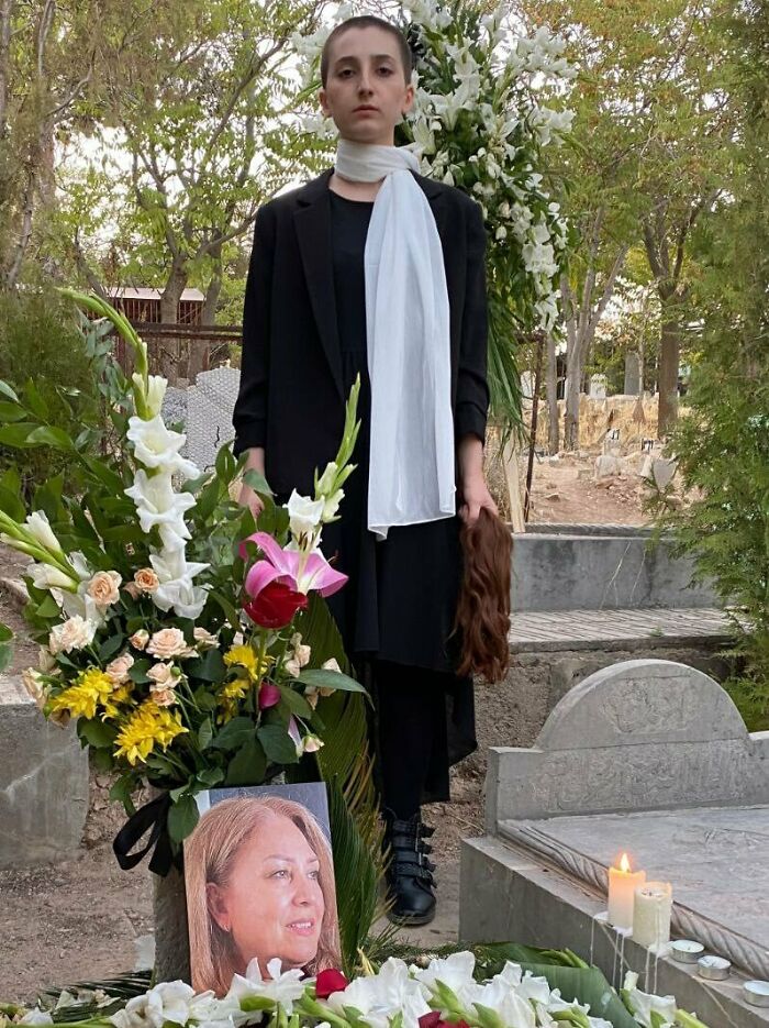 The Daughter Of Minoo Majidi--A Mother Of Two Who Was Killed By The Iranian Regime While Protesting For Mahsa Amini--Stands At Her Mother's Gravesite. She Is Defiantly Unveiled, And In Her Left Hand She Holds The Hair She Cut From Her Head