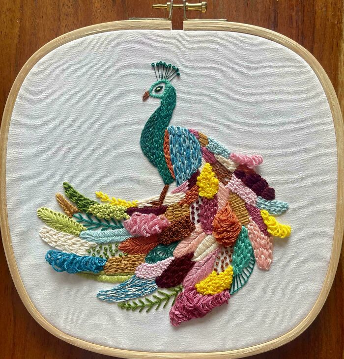 Creative embroidery of a colorful peacock in a hoop, showcasing detailed and vibrant stitching.