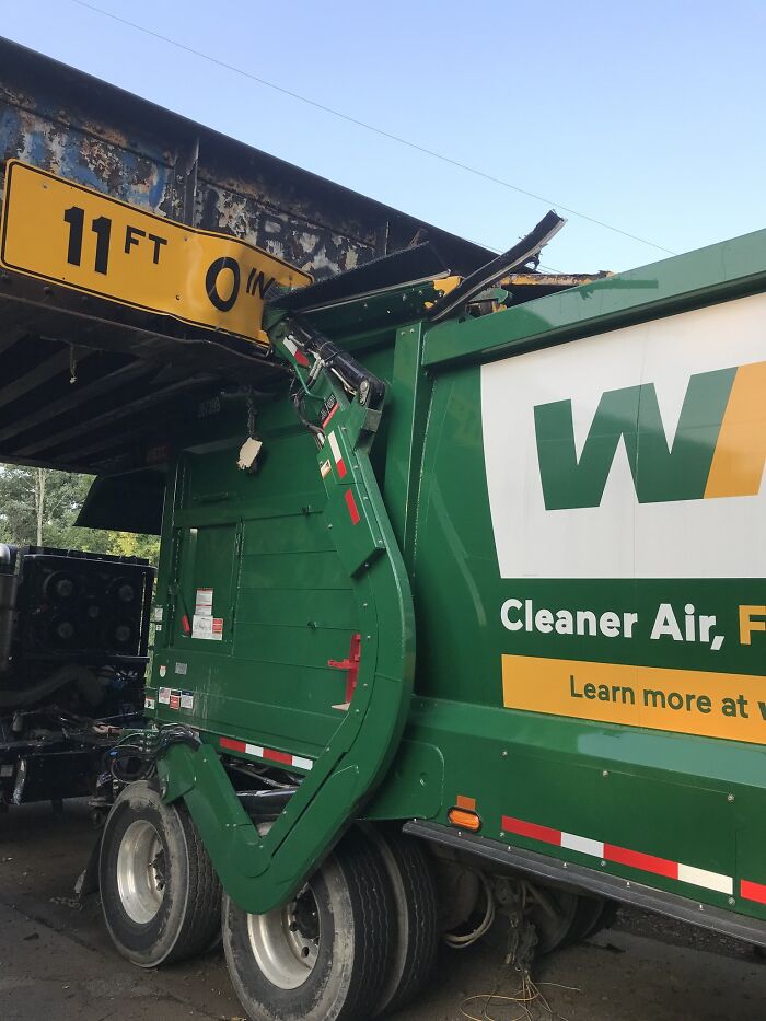 Garbage truck stuck under an 11-foot bridge, showing unfortunate incident likely costing a fortune in damages.