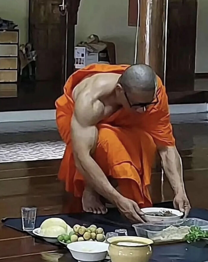 A monk in orange robes, showcasing absolute units of muscle, serves food on the floor.