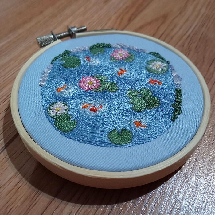 Creative embroidery of a pond with koi fish and lilies displayed in a wooden hoop.