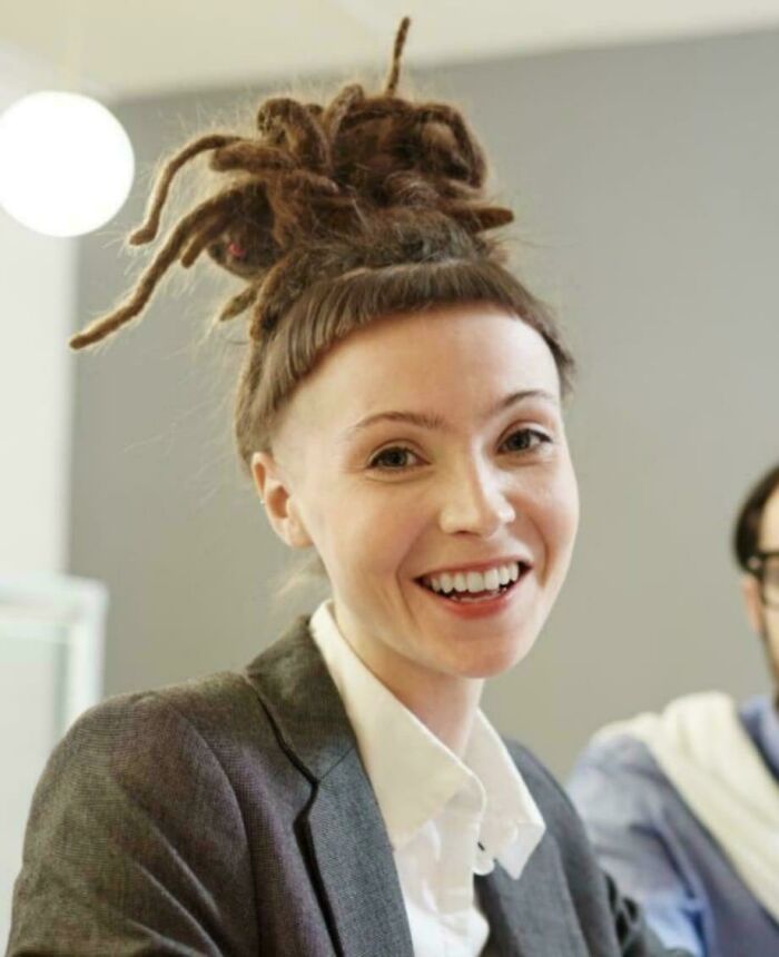 Woman with a unique hairstyle, dreadlocks styled upwards, smiling in a professional setting.