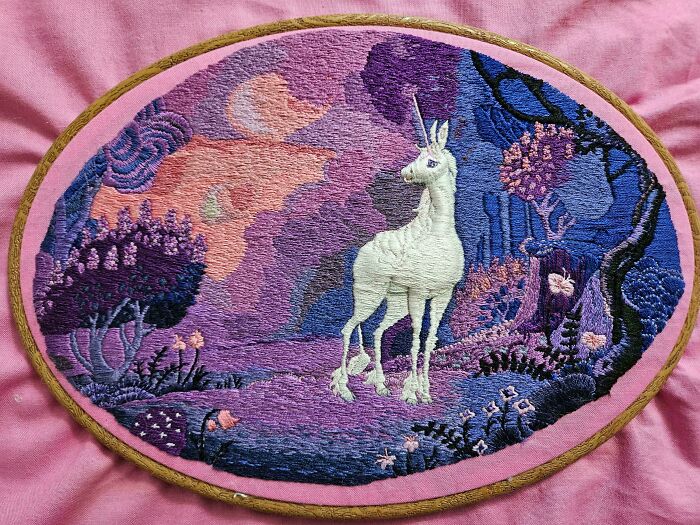 Creative embroidery of a unicorn in a vibrant, mystical forest with purple and pink hues.