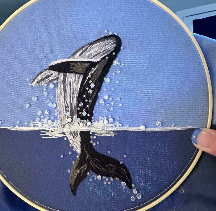 Creative embroidery art depicting a whale breaching, with intricate detail and vibrant colors on a blue fabric.