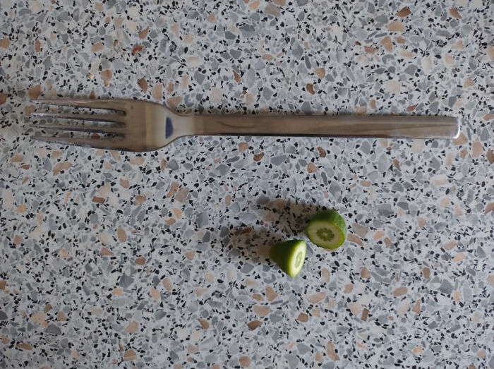 Tiny green fruit next to a fork on a speckled surface, highlighting a gardening attempt with a small harvest.