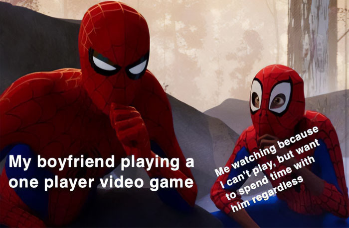  A love meme featuring two characters dressed as Spider-Man sitting together. The larger Spider-Man is labeled, "My boyfriend playing a one player video game." The smaller Spider-Man, who is watching attentively, is labeled, "Me watching because I can't play, but want to spend time with him regardless." The background shows a rocky, outdoor scene.