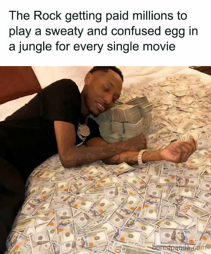 A The Rock meme featuring an image of a man lying on a bed covered with stacks of cash, embracing the money with a satisfied expression. The text above reads, "The Rock getting paid millions to play a sweaty and confused egg in a jungle for every single movie," humorously exaggerating The Rock’s frequent roles in jungle-themed films and comparing his success to someone literally sleeping in money. The meme playfully mocks the repetitive nature of his roles while highlighting his lucrative career.