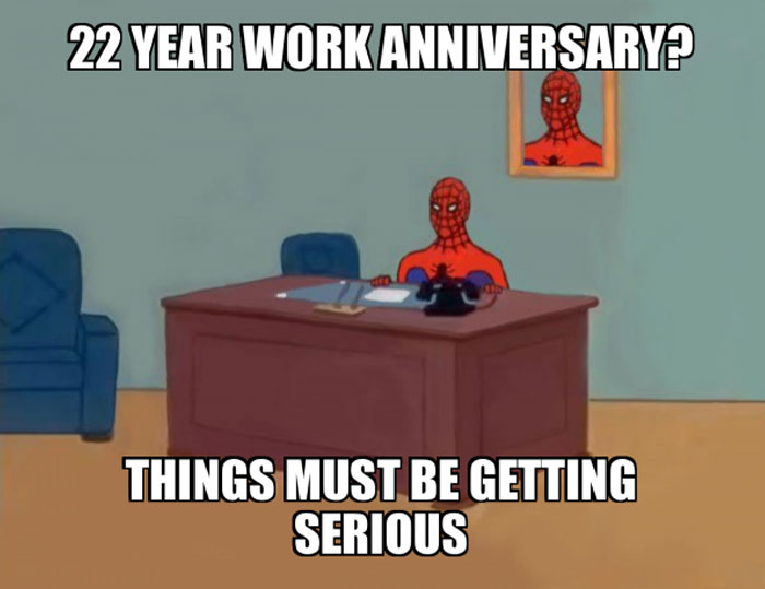 A work anniversary meme featuring an image from the classic Spider-Man cartoon. Spider-Man is sitting at a desk in an office with a picture of himself hanging on the wall behind him. The text at the top reads, "22 YEAR WORK ANNIVERSARY?" and the text at the bottom says, "THINGS MUST BE GETTING SERIOUS." The meme humorously comments on the long duration of employment, implying that such a lengthy tenure is a significant commitment.