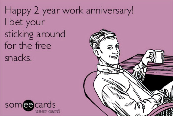 A Work Anniversary meme designed in the style of a someecards image. It features a man casually sitting and holding a mug, with a smirk on his face. The text on the image reads, "Happy 2 year work anniversary! I bet you're sticking around for the free snacks." The meme humorously suggests that the main motivation for staying at a job might be the free food provided by the company.