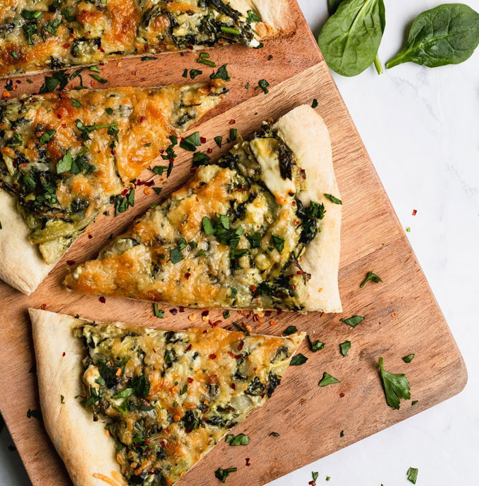 A lunch idea featuring spinach artichoke flatbread slices topped with melted cheese and herbs, arranged on a wooden cutting board.