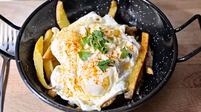 A Lunch idea featuring a skillet with crispy fries topped with poached eggs, garnished with parsley and sprinkled with paprika.