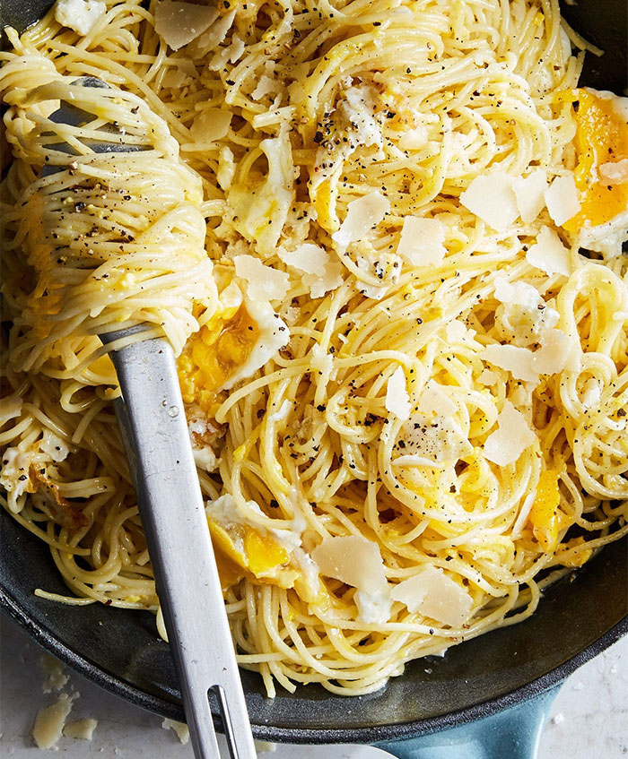 A Lunch idea featuring spaghetti mixed with fried eggs, topped with shaved Parmesan cheese and freshly ground black pepper.