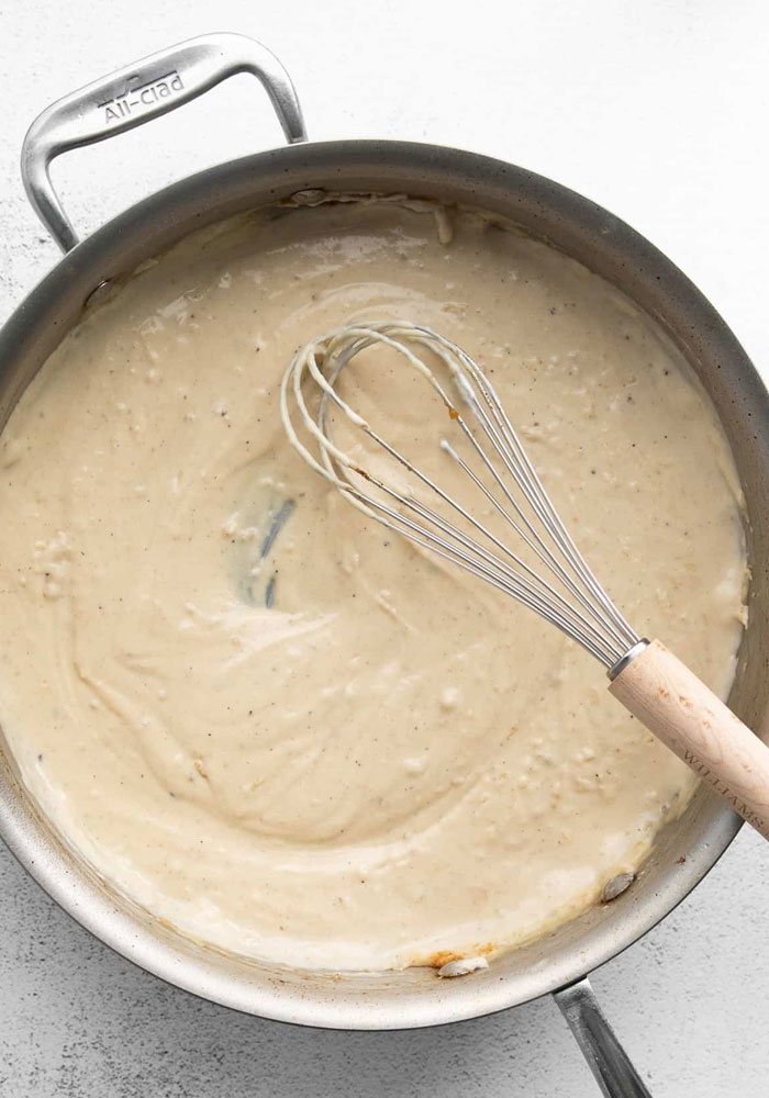 A lunch idea featuring a creamy garlic Alfredo sauce being whisked in a stainless steel pan, ready for adding to a delicious meal.