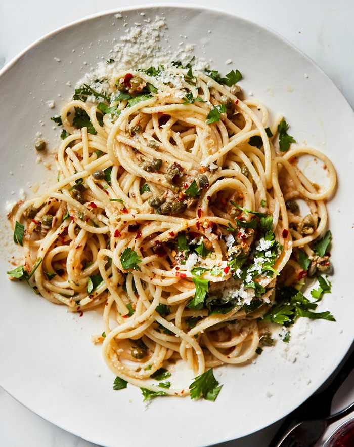 A Lunch idea featuring a plate of spaghetti topped with capers, parsley, grated cheese, and red pepper flakes for a simple yet flavorful meal.