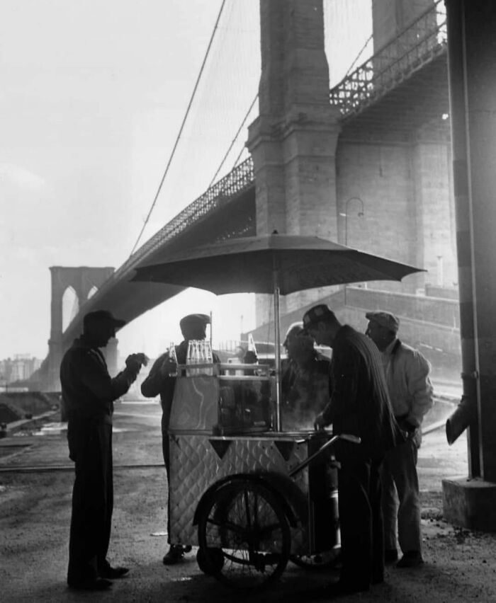 A Group Of Workers Gathered At A Portable Snack Stand Beneath Brooklyn Bridge, Refreshments In Hand, In The 1950s