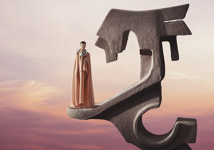 Futuristic photograph with a person in a flowing gown on a surreal sculpture against a sunset sky.