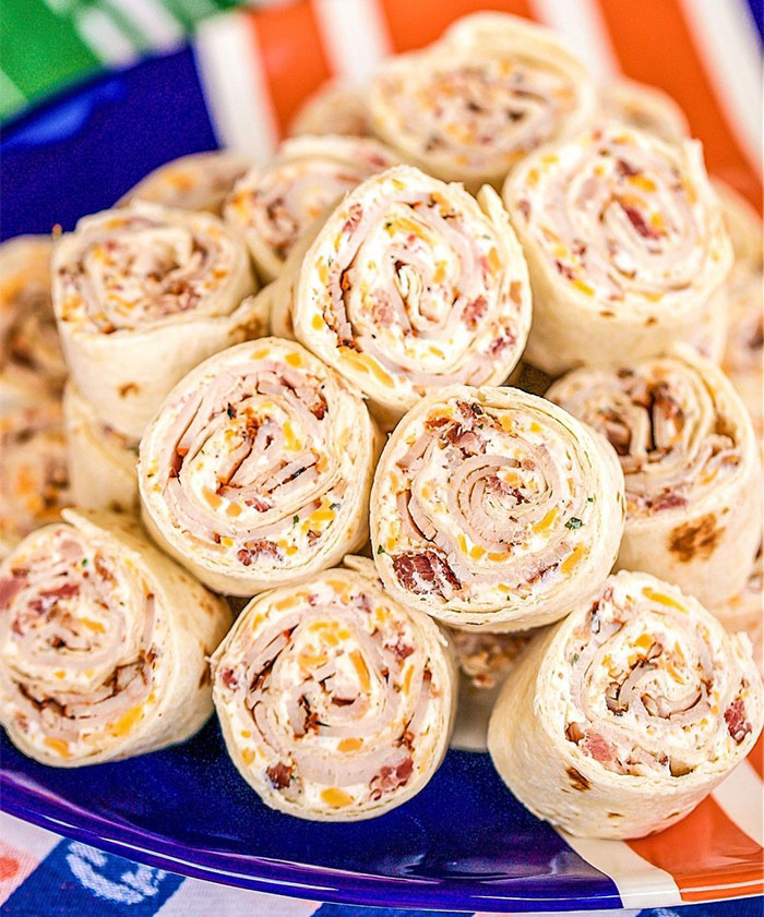 A Lunch idea featuring a plate of tortilla pinwheels filled with cream cheese, bacon bits, shredded cheese, and herbs, served as bite-sized rolls.