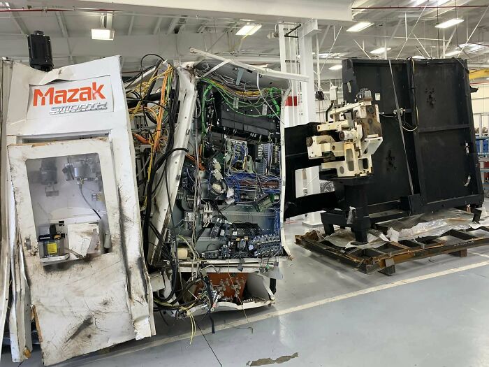 Damaged industrial machine in a factory, showing exposed wires and panels after an unfortunate incident.