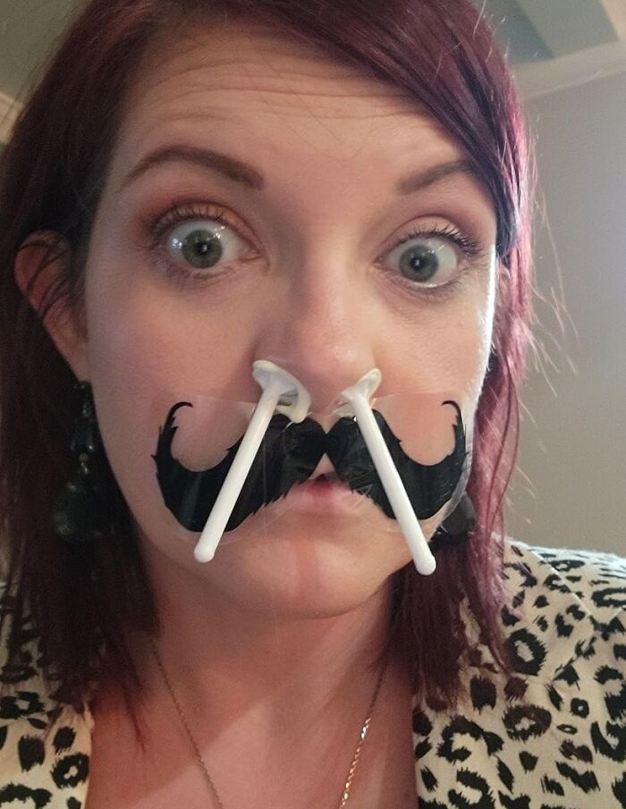 Woman with a playful fake mustache made of cotton swabs, embodying disguise humor suitable for a plain brown box delivery.