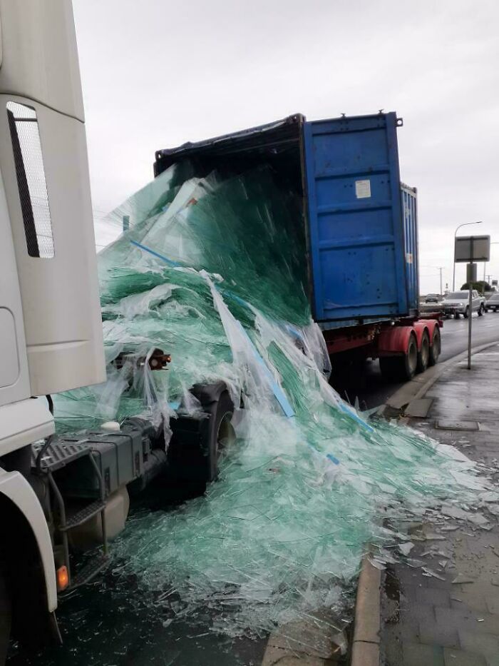 Truck accident with shattered glass spill, highlighting unfortunate incident and expensive damage on wet road.