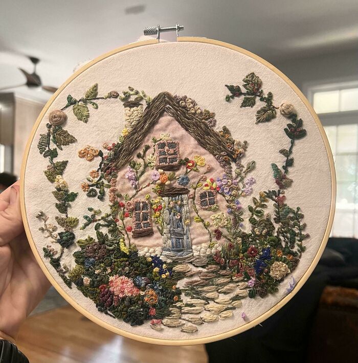 Creative embroidery art featuring a detailed cottage and garden in a hoop.