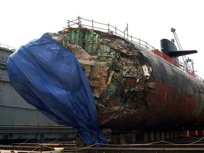 Damaged submarine covered with tarp, indicating an unfortunate incident likely leading to costly repairs.