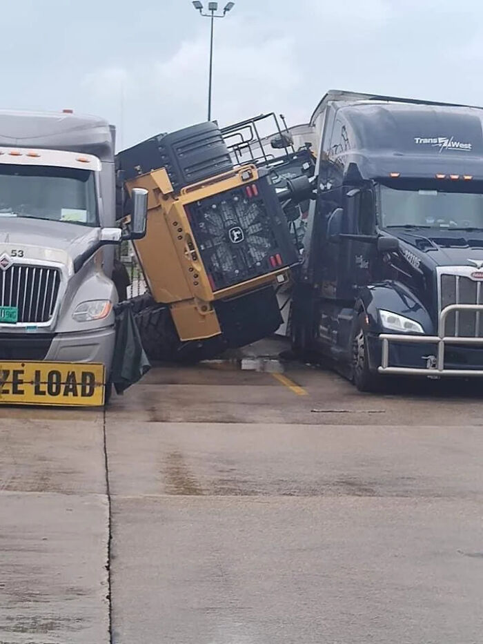 Trucks in a parking lot with a fallen digger between them, suggesting an unfortunate expensive incident.