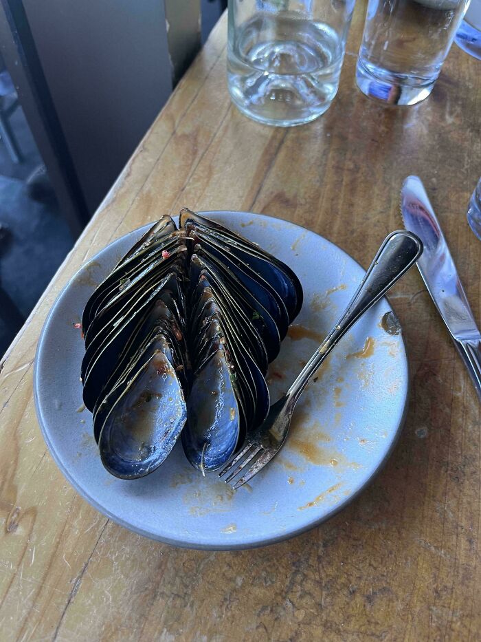 Mildly interesting display of stacked mussel shells on a plate with fork and knife.