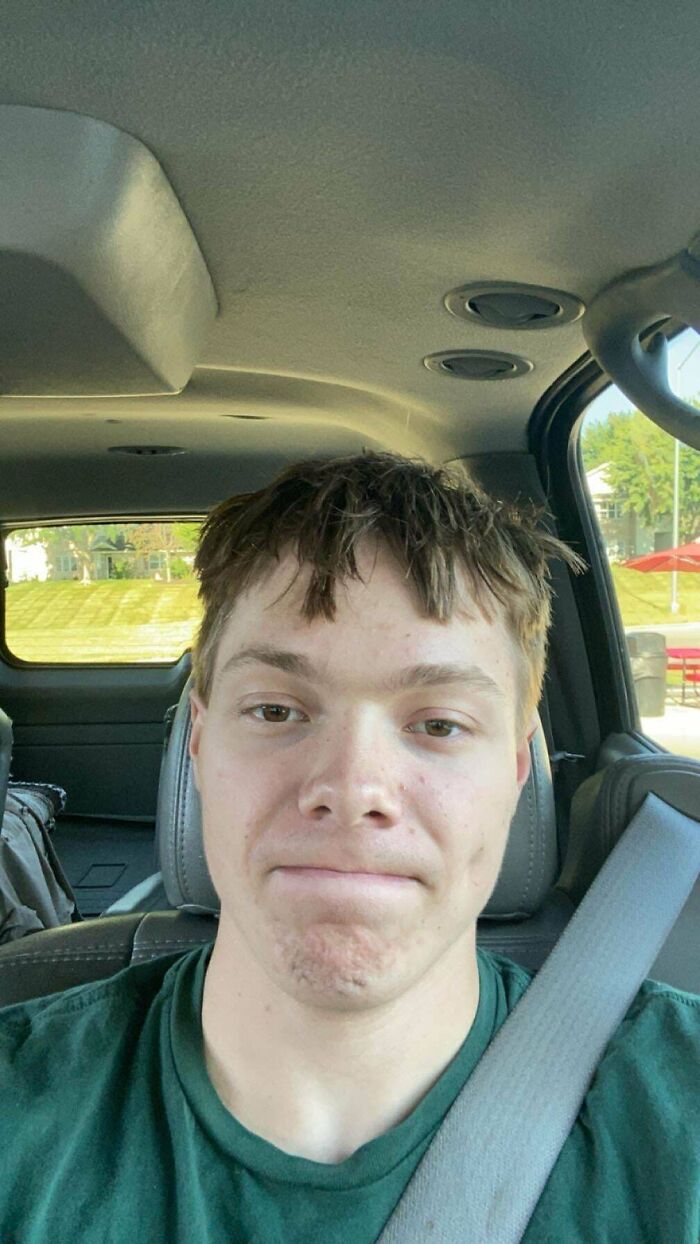 Person with a tragic hair accident, sitting in a car, wearing a green shirt and seatbelt.