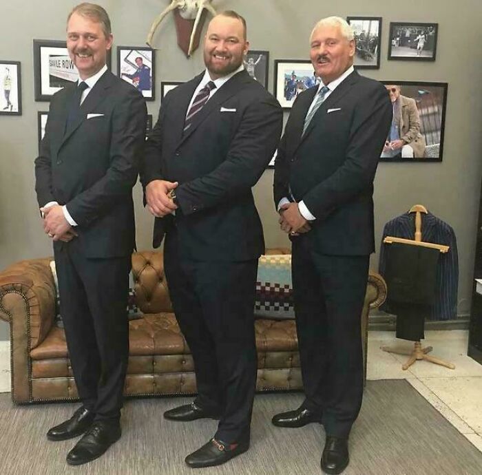 Three men in suits standing in an office, showcasing absolute units of style and stature.