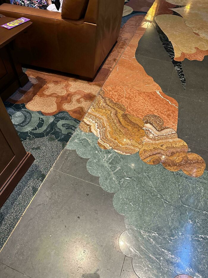 Mildly interesting pattern of colorful stone and carpet blending on a floor near a brown couch.