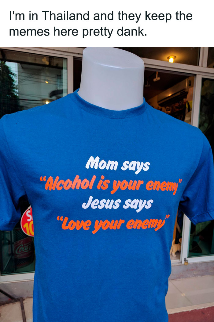 A Christian meme showing a mannequin wearing a blue T-shirt displayed in a shop. The text on the T-shirt reads: "Mom says 'Alcohol is your enemy'" "Jesus says 'Love your enemy'" Above the image, a caption says, "I'm in Thailand and they keep the memes here pretty dank." The meme humorously combines a mother's advice against drinking alcohol with a biblical teaching to "love your enemy," creating a playful contradiction.