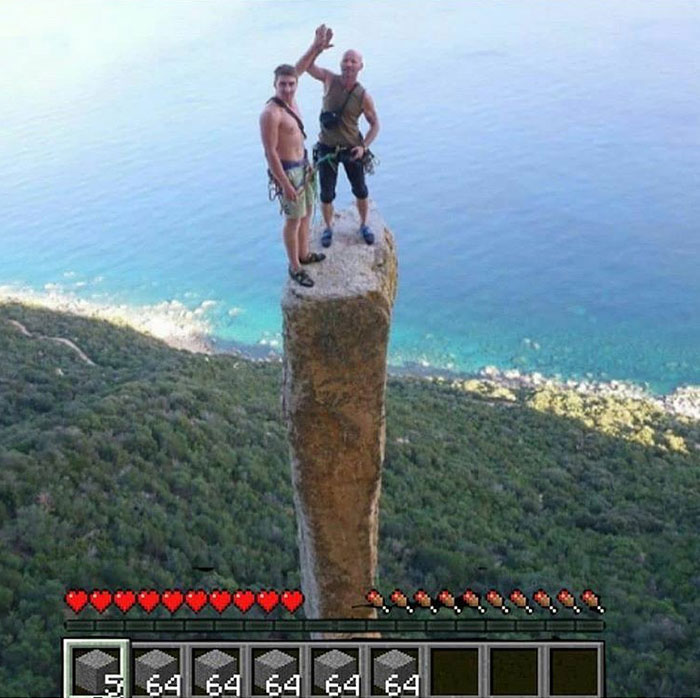 A Minecraft meme showing a real-life photo of two climbers standing on top of a tall, narrow rock pillar with a steep drop around them. The bottom of the image is edited to include the Minecraft game interface, displaying the player's health bar, hunger bar, and an inventory filled with stone blocks. The meme humorously makes it look like the climbers are standing on a single block tower that one might build in Minecraft, playing on the game's physics and building mechanics.