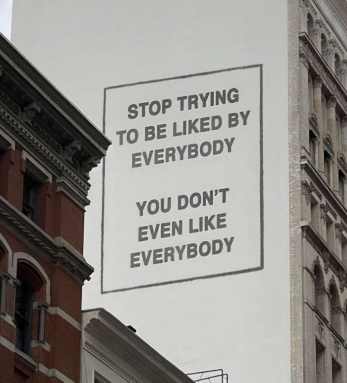 A motivational meme on a building wall reads, "Stop trying to be liked by everybody. You don't even like everybody," in bold black letters.