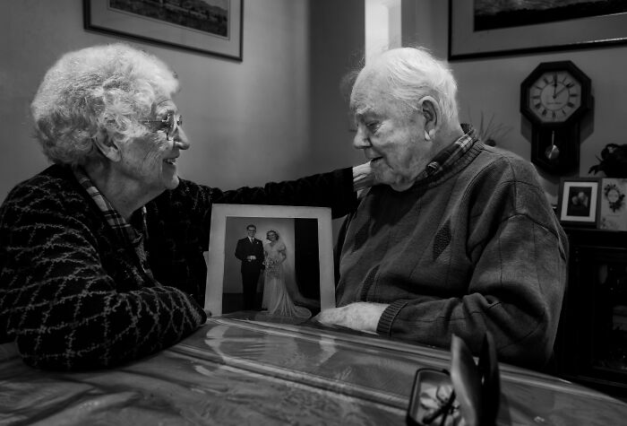 Elderly couple sharing a joyful moment with a wedding photo, a winning image at Tokyo International Foto Awards 2023.